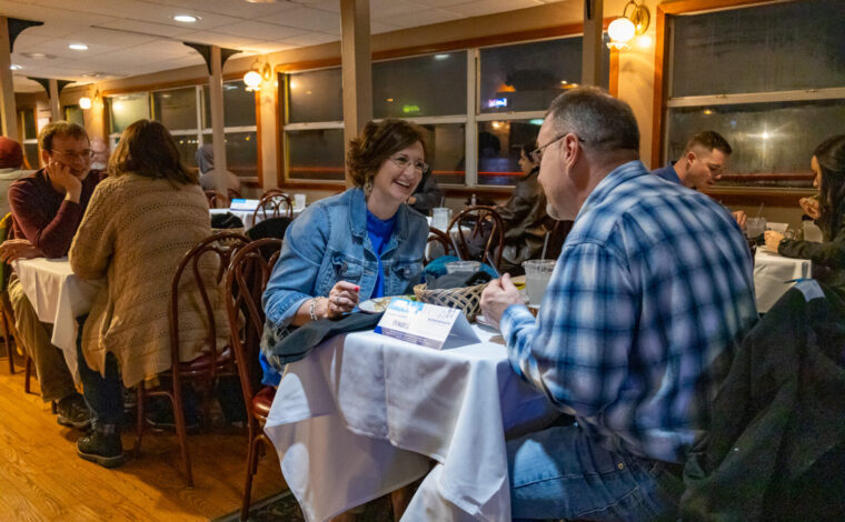 A couple smiles while eating at a table on a Skyline Dinner Cruise